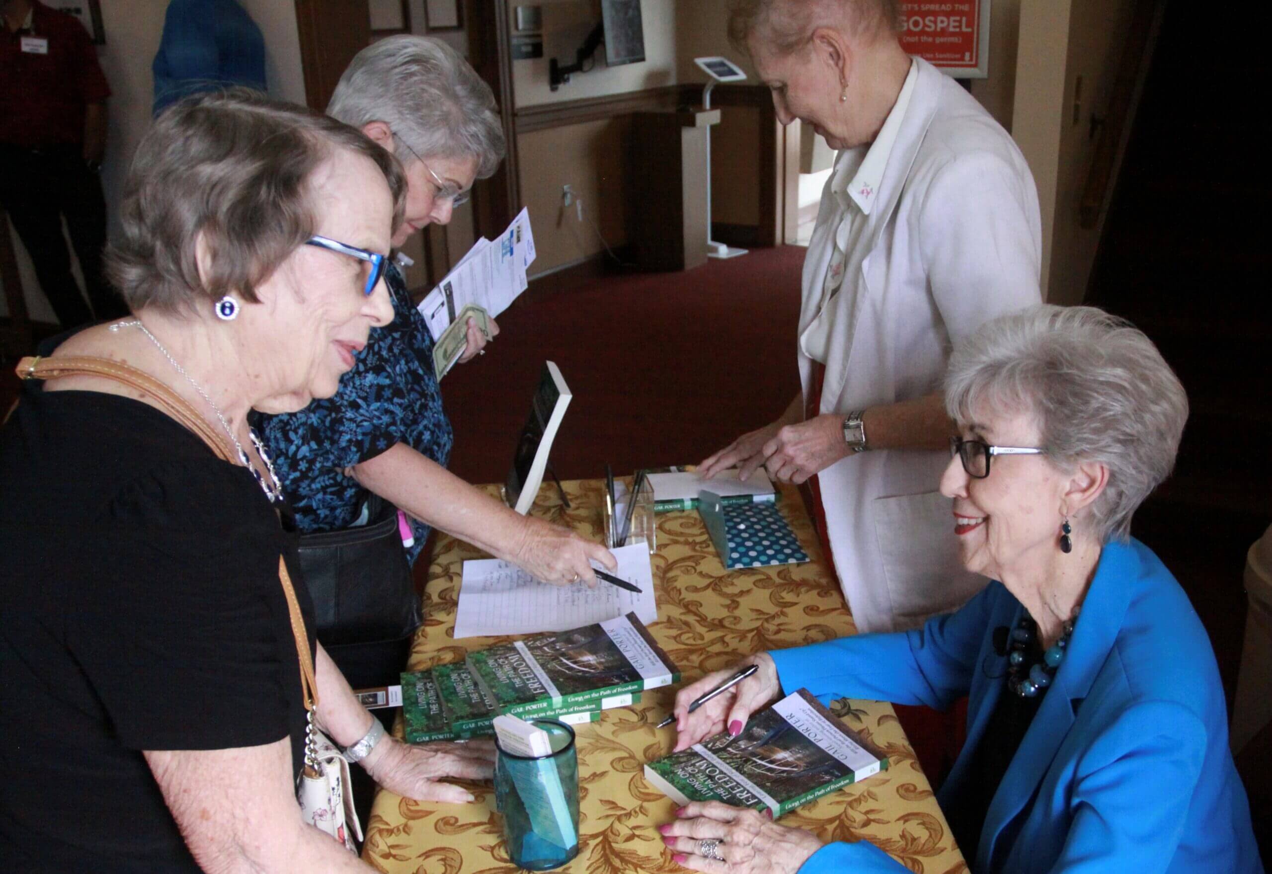 A group of older women at a table signing books.