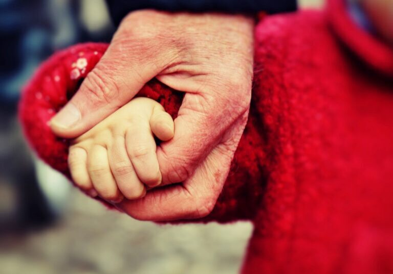 An adult holding a child's hand tenderly.