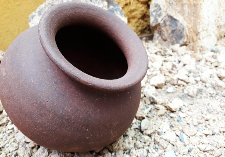 Close-up of an empty rustic clay pot on rocky ground.