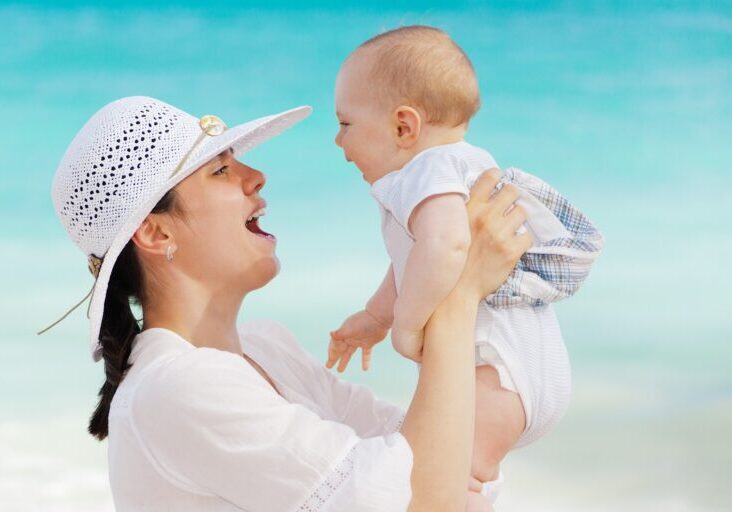 Mother joyfully lifting baby on a sunny beach.