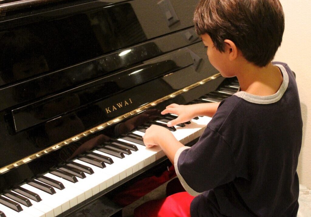 A young boy playing a grand piano with focused attention.