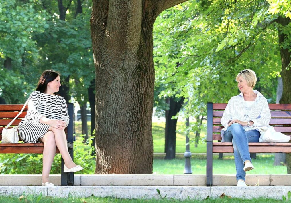 Two women sitting on separate benches in a park, engaged in conversation.